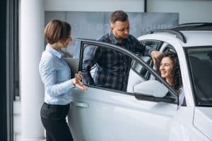 Smiling couple speaking with a saleswoman at a dealership while exploring a white SUV, illustrating the customer experience in car financing.