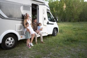 A happy family of four enjoys a moment outdoors beside their motorhome, highlighting the freedom and adventure associated with recreational vehicles in nature settings.