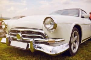 A close-up view of a vintage white convertible with chrome detailing parked on grass, showcasing the timeless design typical of classic and collector cars.