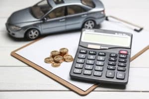 A black calculator, stacked coins, and a miniature car placed on a clipboard, symbolizing budgeting and planning for car financing decisions.