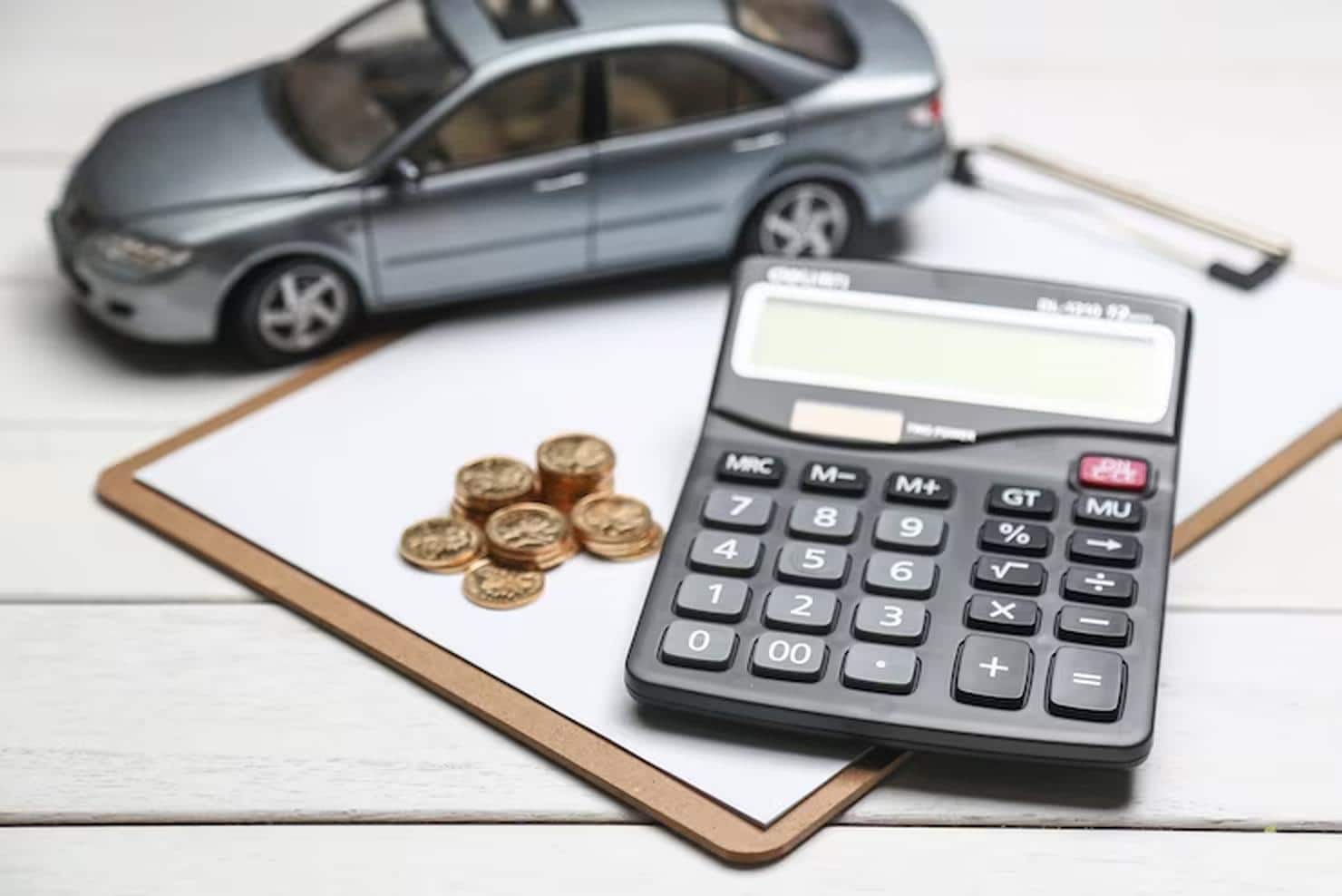 A black calculator, stacked coins, and a miniature car placed on a clipboard, symbolizing budgeting and planning for car financing decisions.