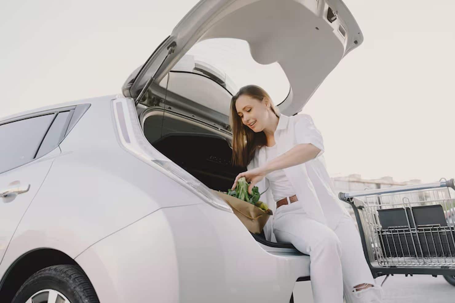 Woman loading groceries into the trunk of a white car in a parking lot, symbolizing the convenience and accessibility offered by Special car financing programs for everyday consumers.