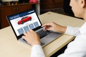 A man browsing a car service website on a laptop, viewing details of a red sports car, representing the online process of exploring car financing options.