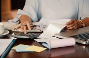 Person using a calculator and analyzing financial documents at a desk with a laptop and sticky notes, illustrating the Values-Based Budgeting Trend focused on aligning spending with personal priorities and goals.