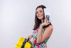 Smiling woman holding flight tickets and a credit card next to a yellow suitcase, representing the travel benefits made possible through credit cards with cashback, which help save on purchases and earn rewards.