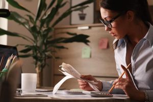 Focused woman analyzing receipts and using a calculator at her desk, representing the process of building a detailed financial plan to manage expenses and improve budgeting strategies.