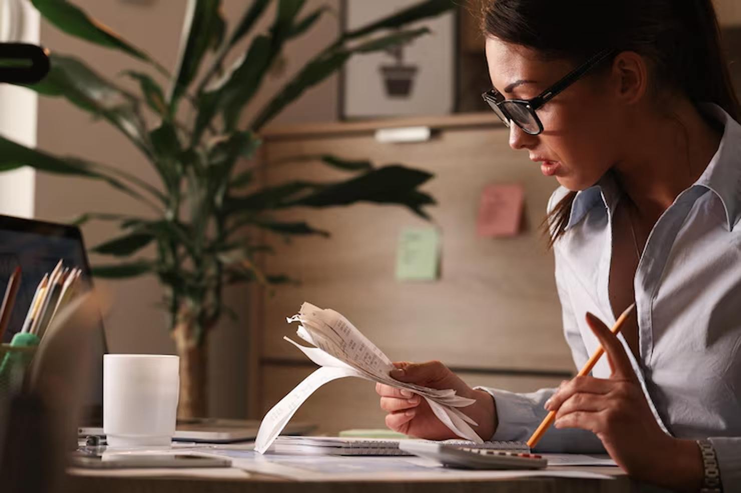 Focused woman analyzing receipts and using a calculator at her desk, representing the process of building a detailed financial plan to manage expenses and improve budgeting strategies.