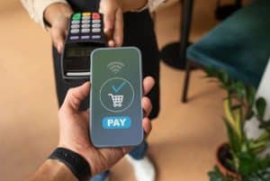 A person holds a smartphone displaying a payment confirmation screen while making a contactless transaction, illustrating the concept of payment automation in a modern retail environment.