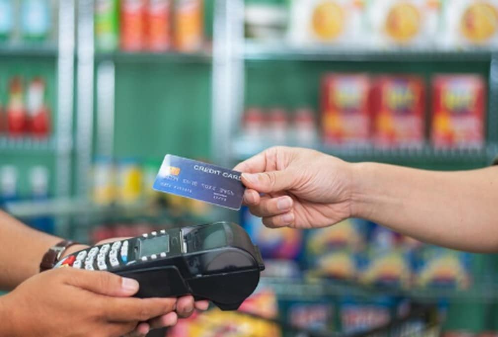 A customer makes a purchase by handing over a reward card to a cashier using a card reader in a grocery store, highlighting the convenience of using reward cards for everyday shopping.