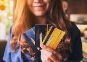 Smiling woman holding three colorful credit cards in her hand, representing the benefits and variety of co-branded credit cards that offer exclusive rewards and loyalty perks for frequent users.