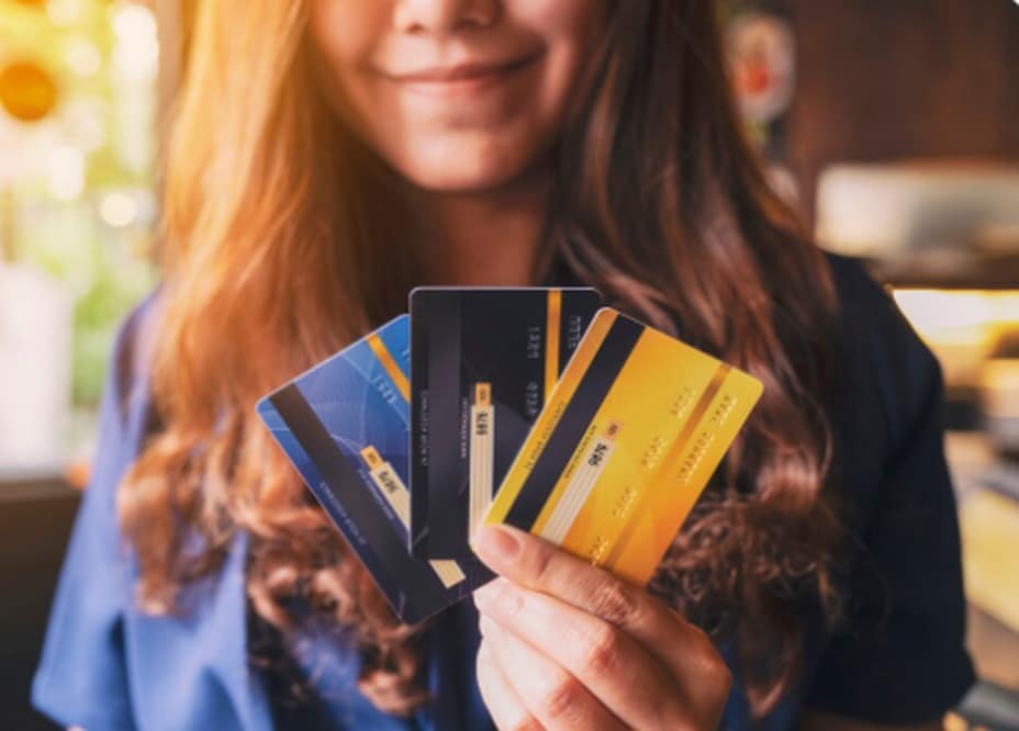 Smiling woman holding three colorful credit cards in her hand, representing the benefits and variety of co-branded credit cards that offer exclusive rewards and loyalty perks for frequent users.