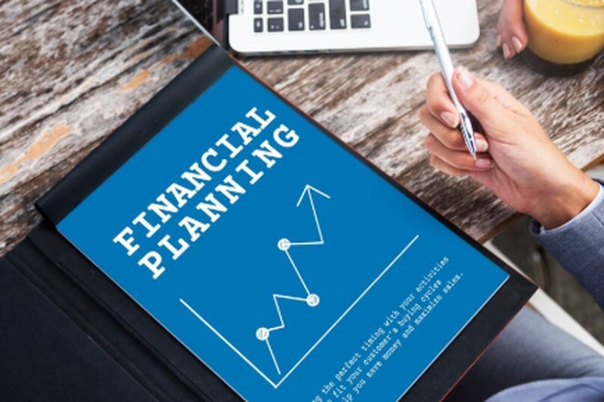Person holding a pen next to a blue document with a chart and the title “Financial Planning,” symbolizing financial planning and the development of sustainable financial habits to achieve long-term economic stability.