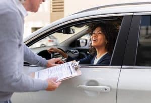 Woman sitting in her car smiling while discussing paperwork with a consultant, representing vehicle financing options and approval process.