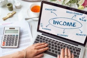 Person working on a laptop with a diagram about income, showing related concepts like financial, investment, funding, economy, and benefit, symbolizing strategies for generating passive income.