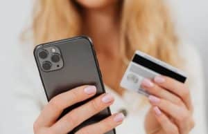 Woman holding a smartphone in one hand and a bank card in the other, illustrating the convenience of credit cards geared toward digital users for online transactions.