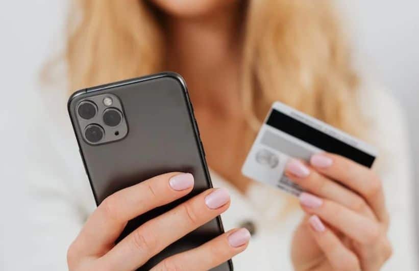 Woman holding a smartphone in one hand and a bank card in the other, illustrating the convenience of credit cards geared toward digital users for online transactions.