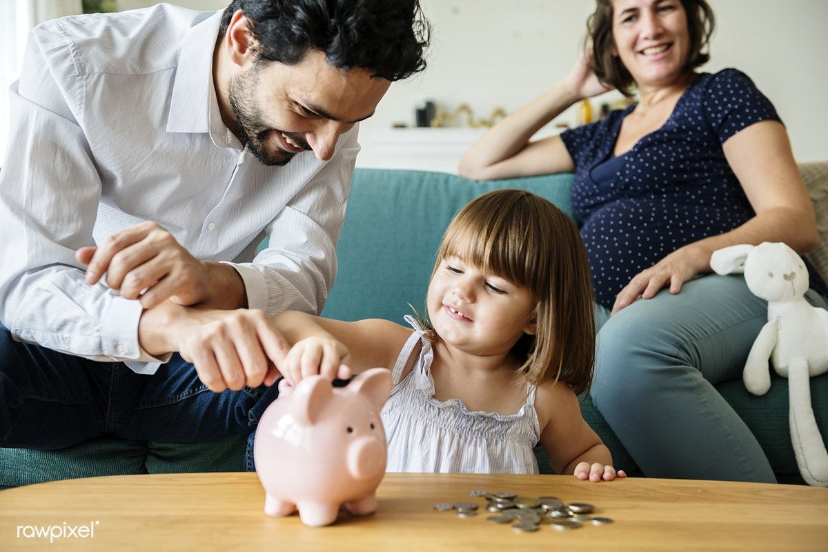 Smiling parents guiding their young daughter as she puts coins into a piggy bank, symbolizing the importance of a family financial plan for building savings and financial security.