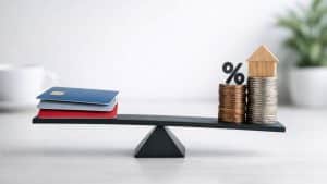 Balance scale with credit cards on one side and stacked coins with house and percentage symbol on the other side